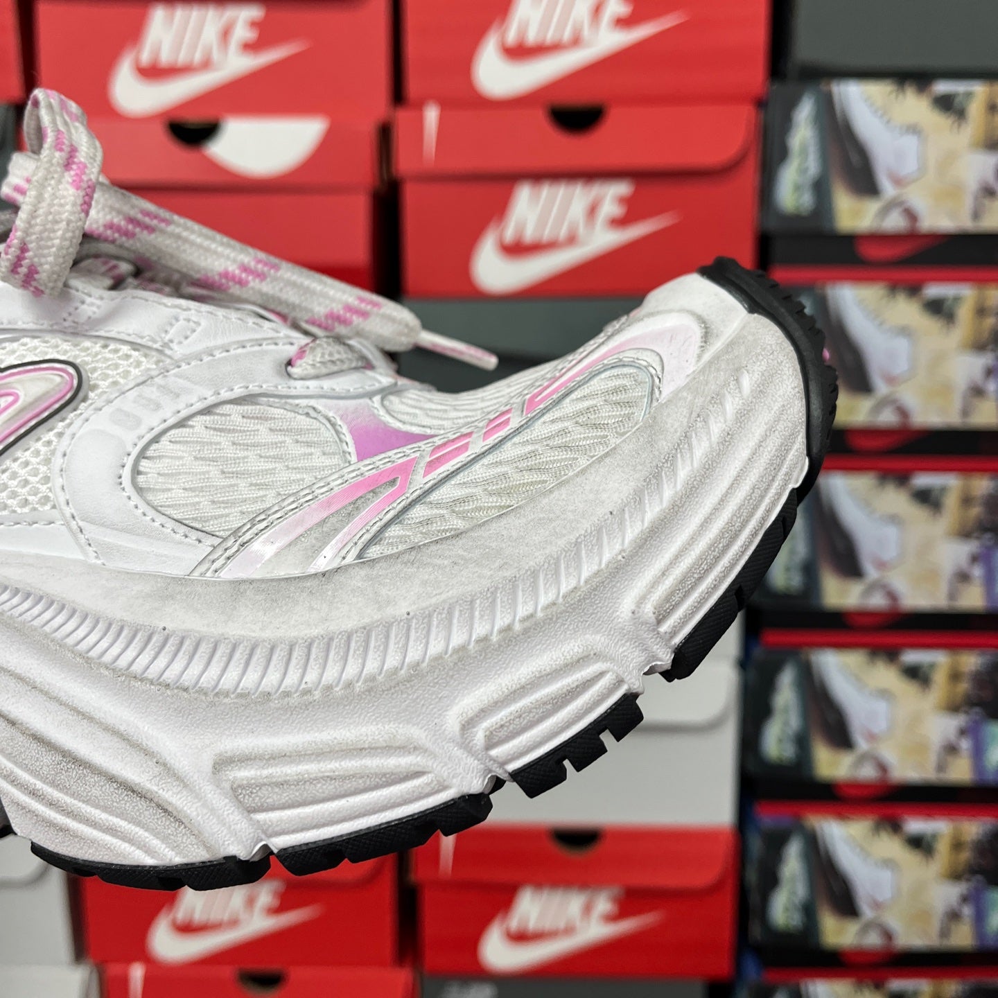 White sneaker side view with black tread outsole and pink accent panels