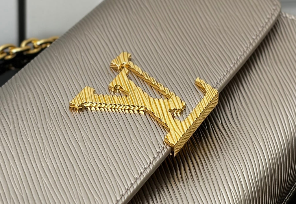 Close-up of gold LV-style logo on textured beige flap