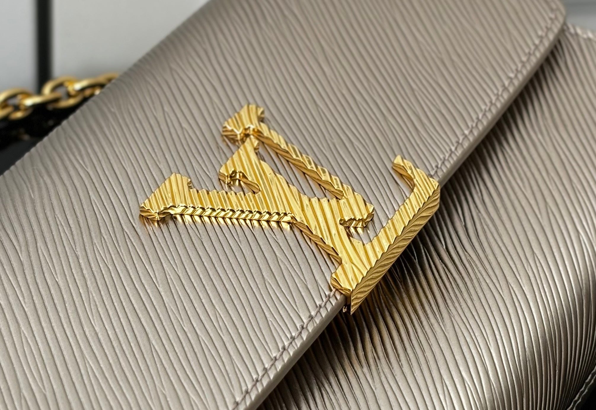 Close-up of gold LV-style logo on textured beige flap