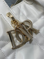 Dior gold logo charm attached to quilted white bag front hardware