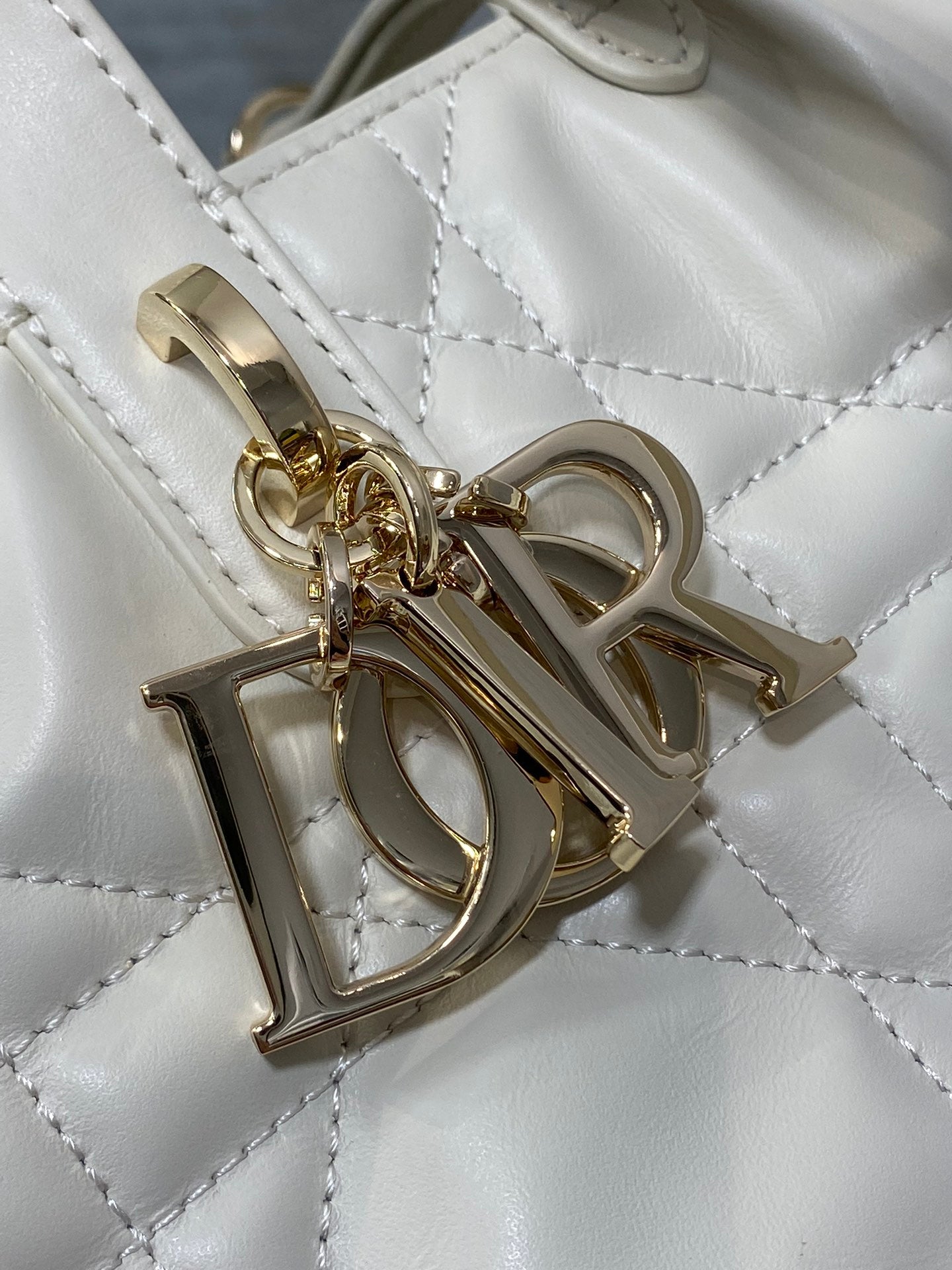 Dior gold logo charm attached to quilted white bag front hardware