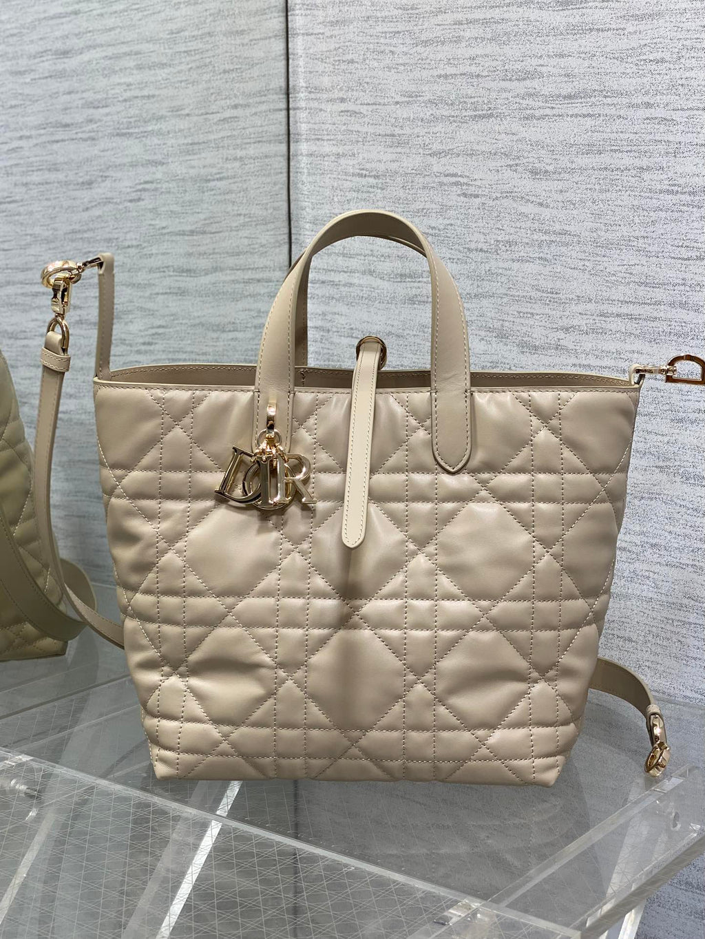Dior cream quilted tote with top handles, front emblem charm, and detachable shoulder strap