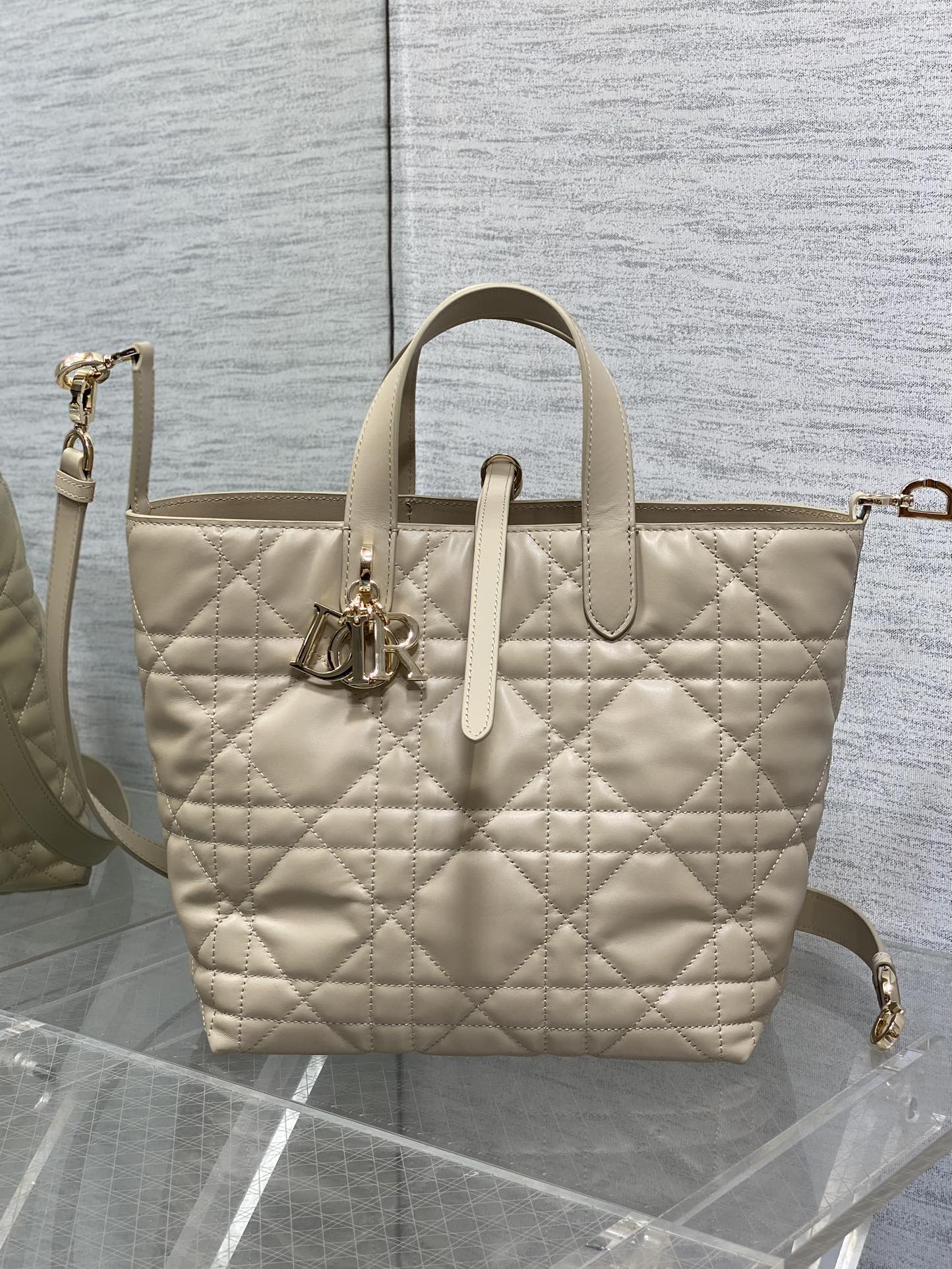 Dior cream quilted tote with top handles, front emblem charm, and detachable shoulder strap