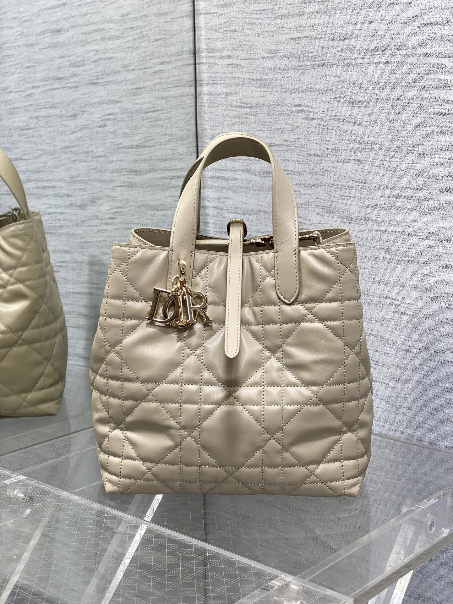 Dior quilted cream handbag with top handles, front charm detail, and zip closure