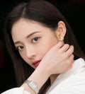 Gold-tone clover flower stud earrings worn by a woman, side view.