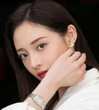 Gold-tone clover flower stud earrings worn by a woman, side view.