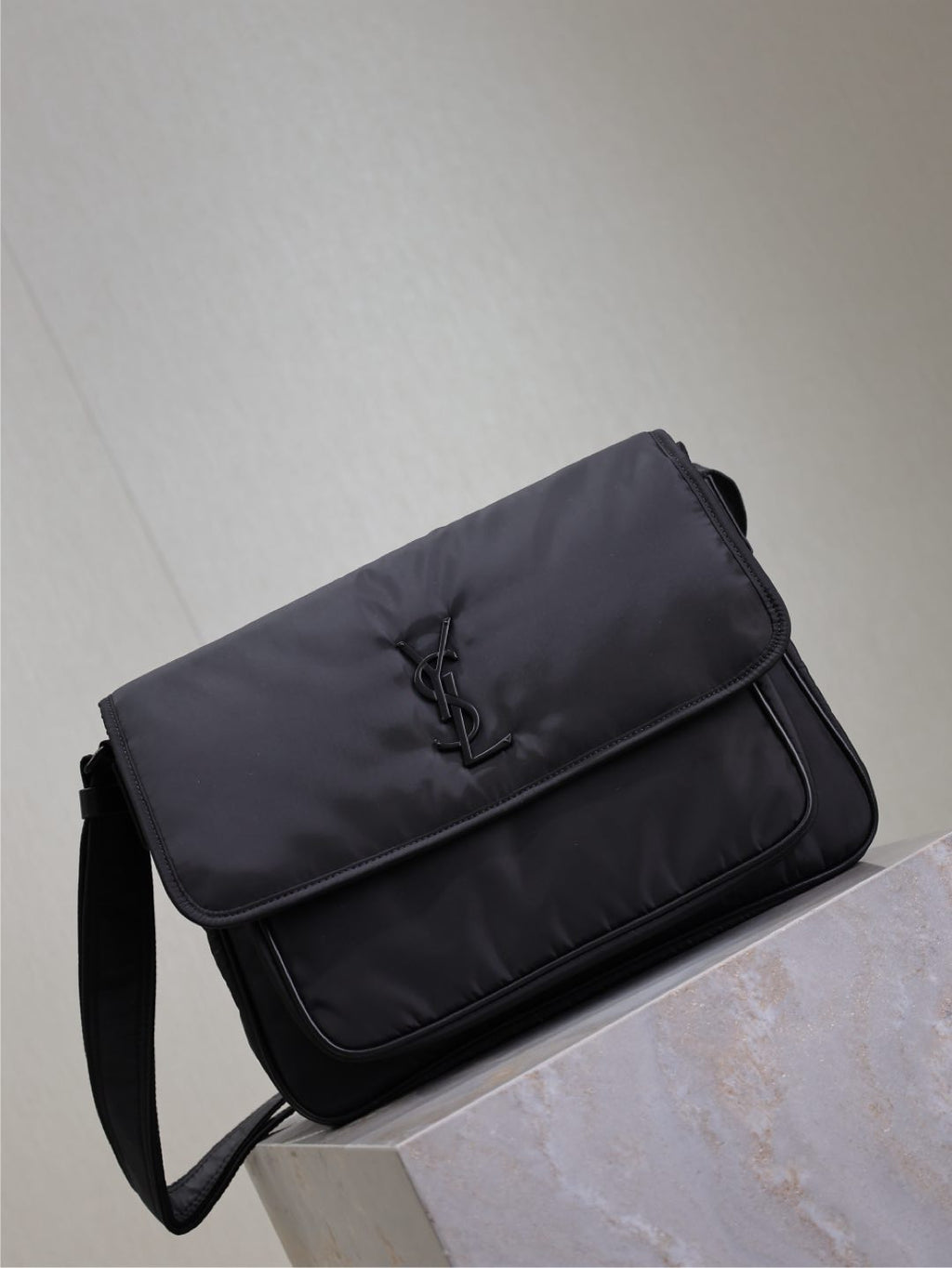 YSL bag side view with front flap and YSL logo, dark padded fabric, shoulder strap