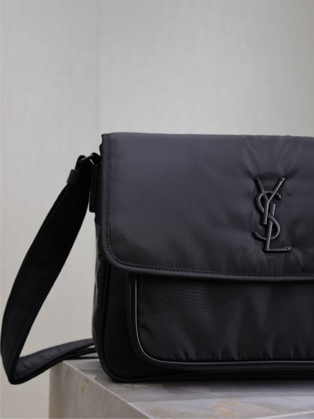 YSL bag close-up of front flap and YSL logo, dark padded fabric, side strap