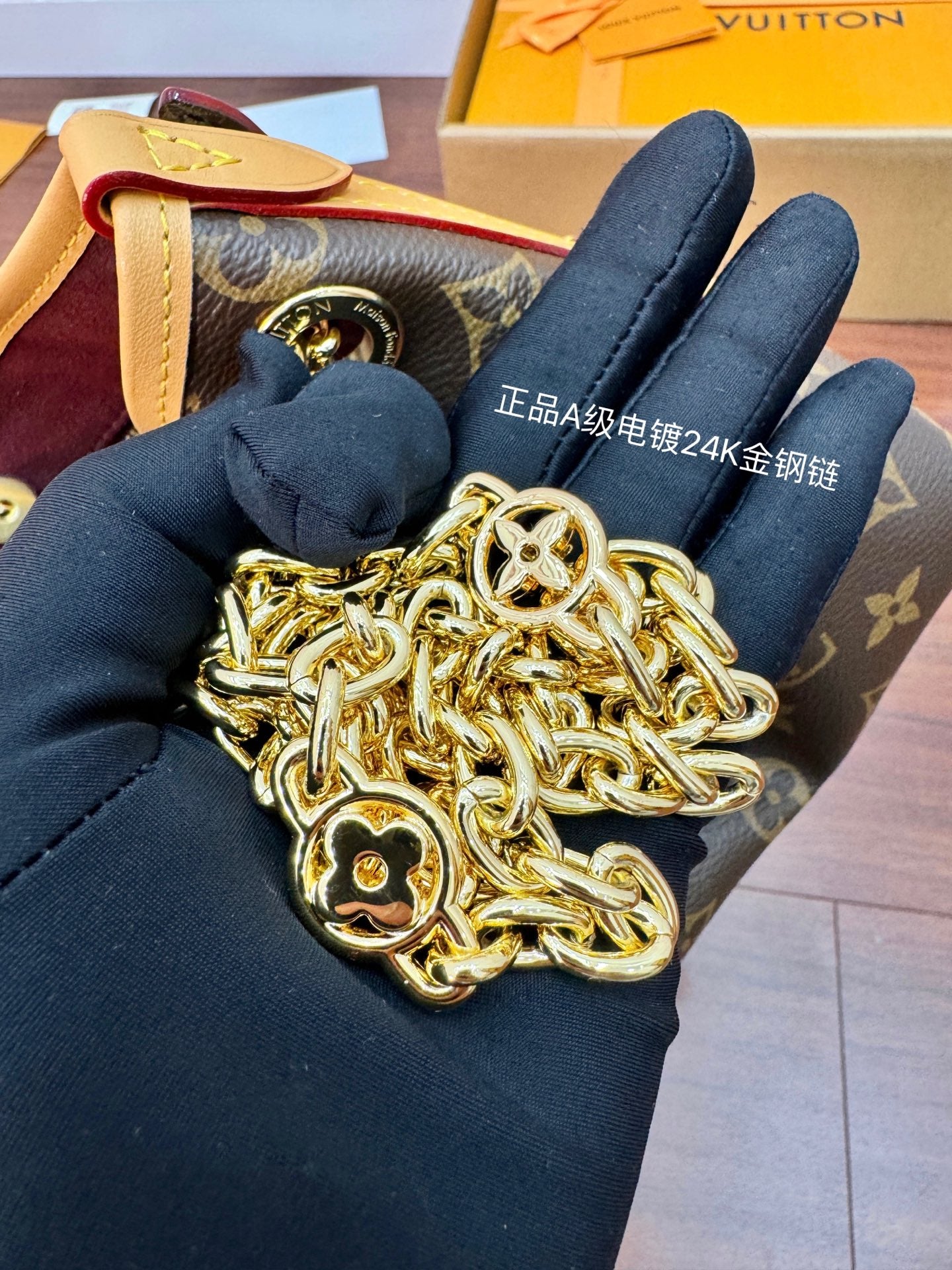 Louis Vuitton gold-tone chain strap in gloved hand attached to monogram bag