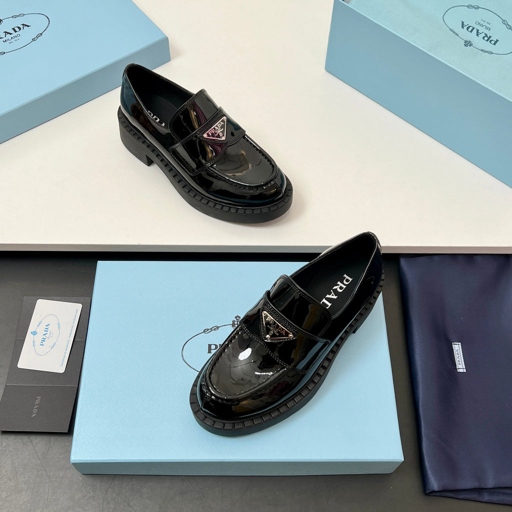 Prada unisex glossy black loafers with buckled strap, gold emblem, and tread sole