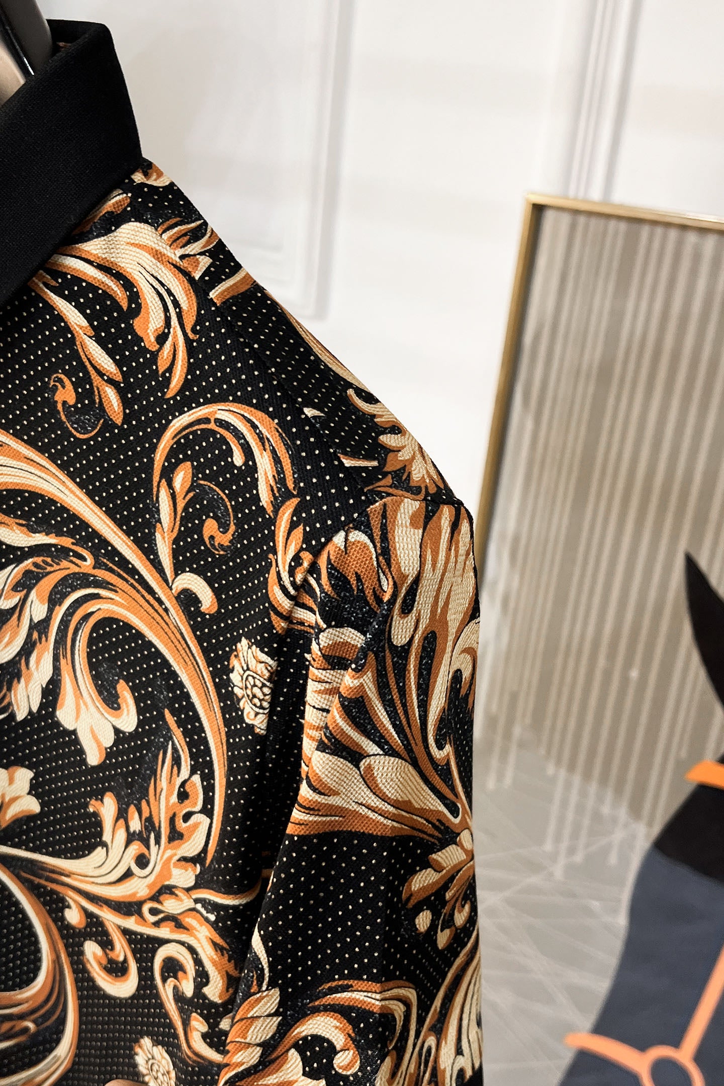 Short-sleeve shirt side view with baroque print on black, gold swirls and short cuff.