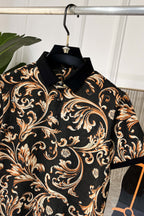 Short-sleeve shirt close-up with high collar and ornate baroque print in black and gold.