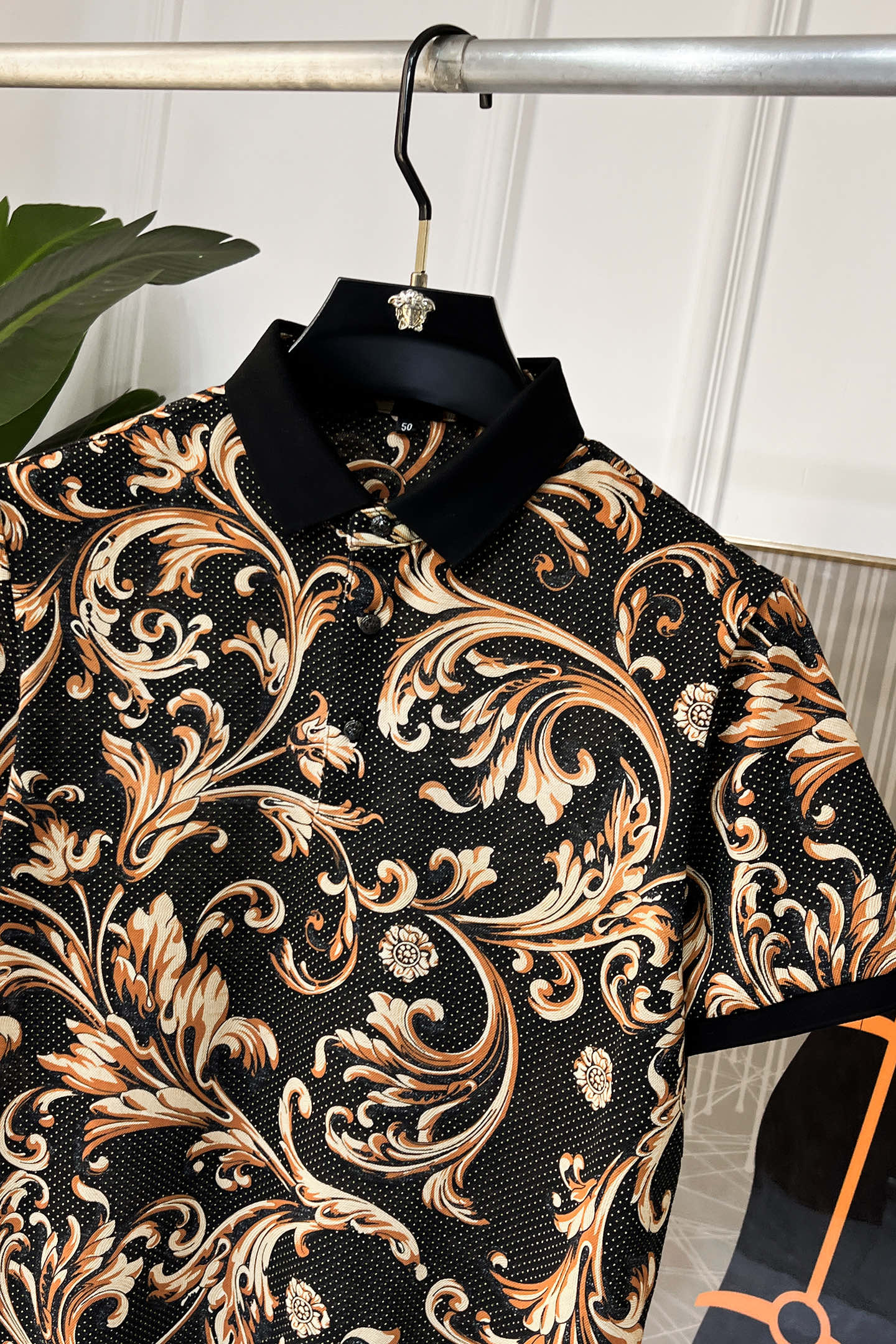 Short-sleeve shirt close-up with high collar and ornate baroque print in black and gold.