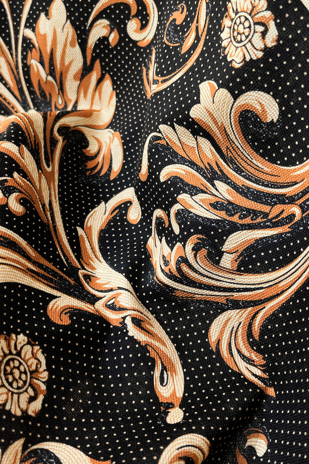 Shirt fabric close-up: black ground with gold-and-orange floral scrolls and tiny dot pattern.