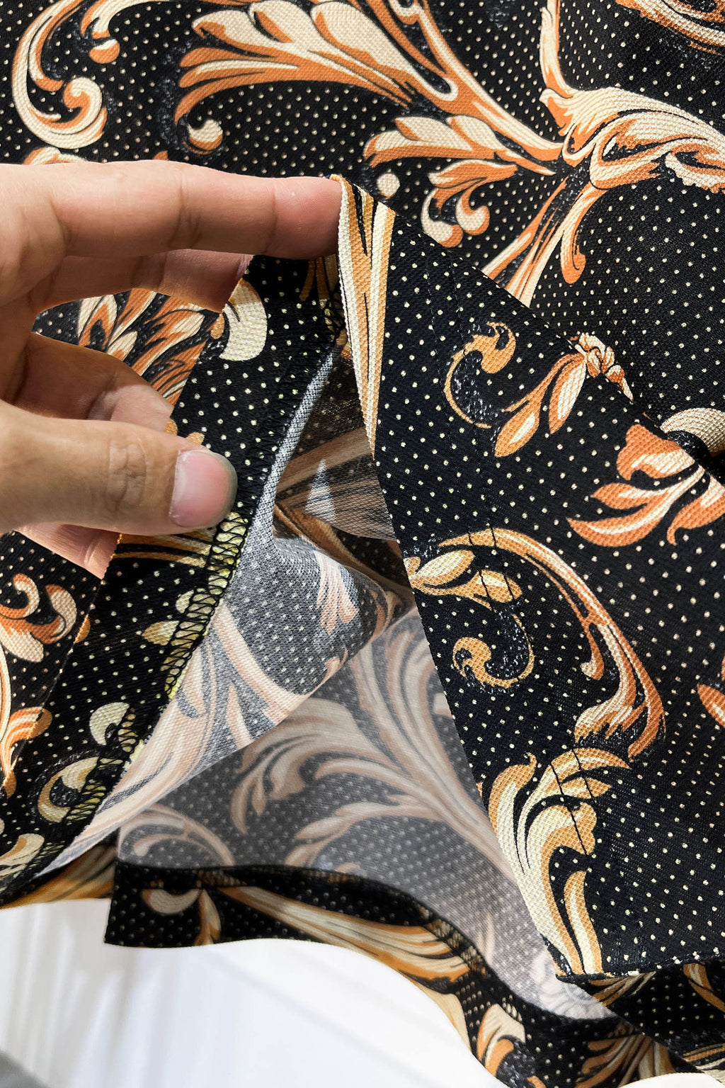 Shirt fabric close-up showing seam and baroque print on black with gold and orange scrolls.