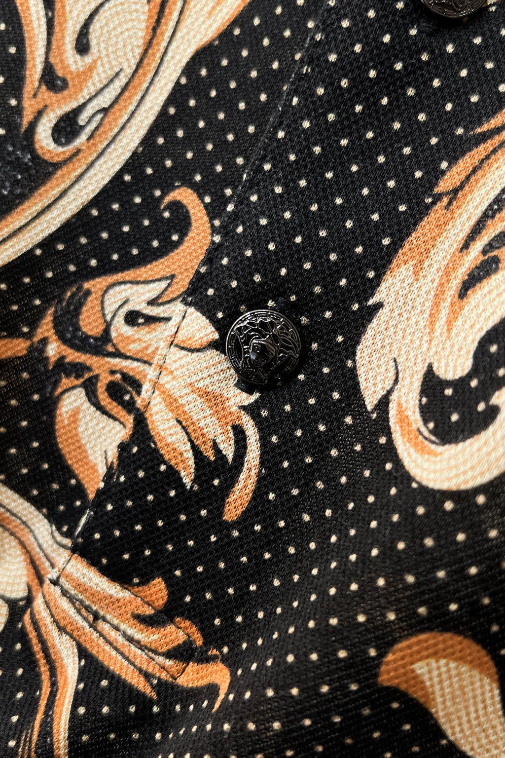 Shirt fabric close-up: black knit with gold and orange swirling motif and dotted accents.