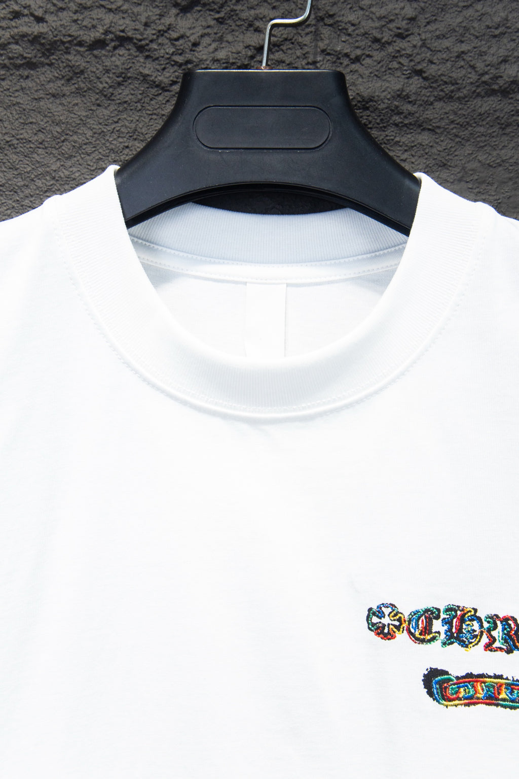 White crew-neck T-shirt close-up with collar seam and small multicolor logo