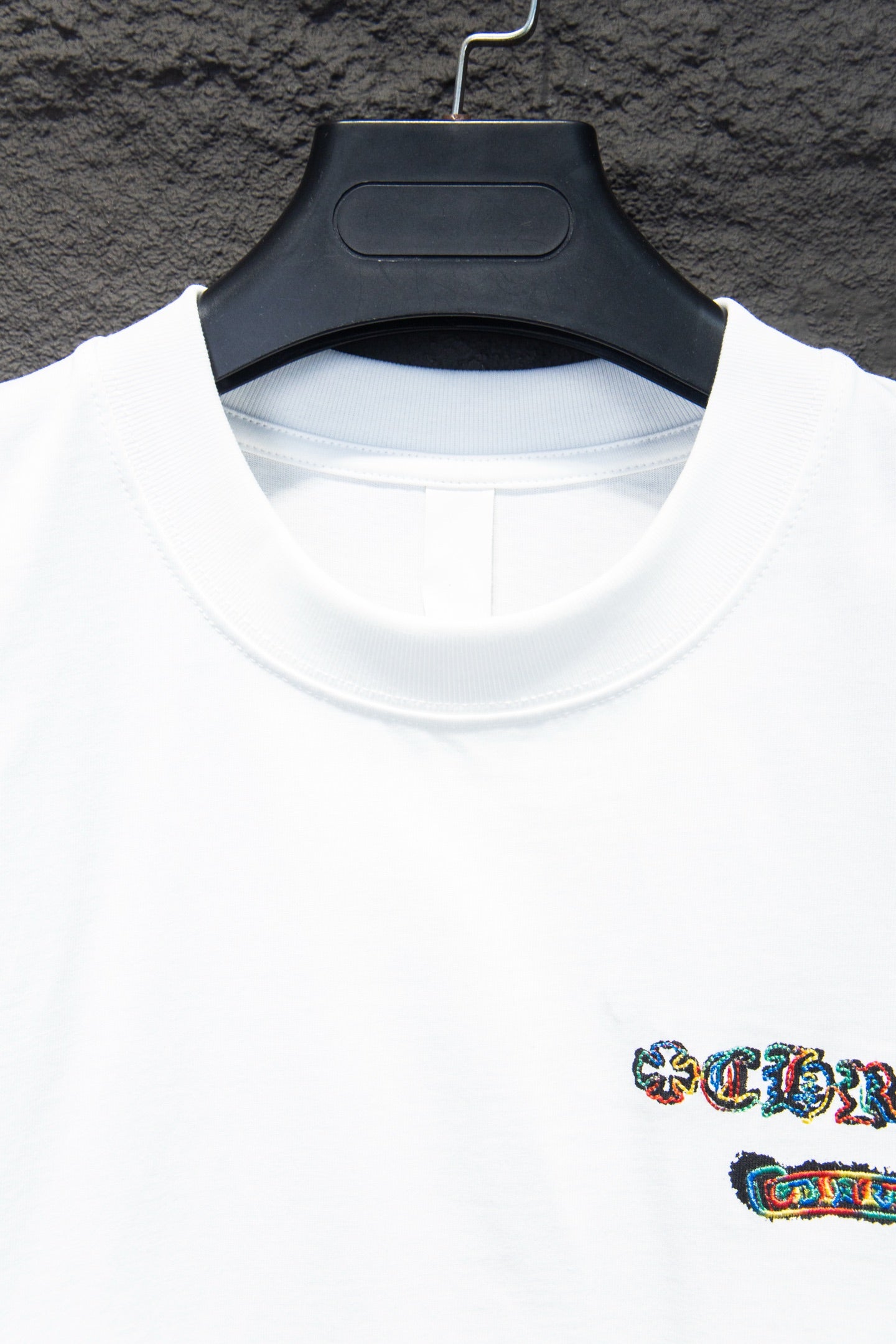 White crew-neck T-shirt close-up with collar seam and small multicolor logo