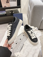 Unisex low-top sneakers held in hand, dark gray uppers with white laces and off-white sole