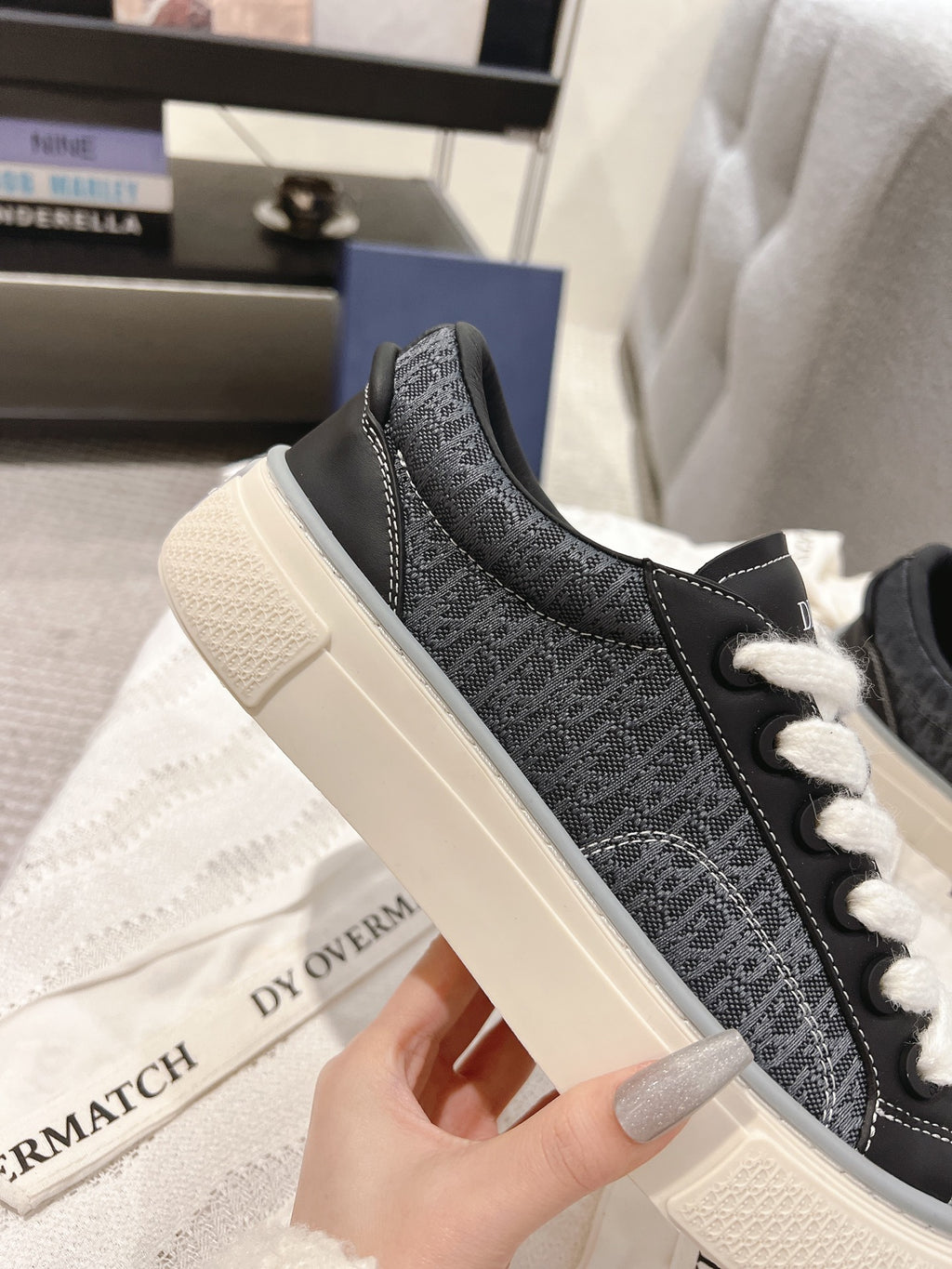 Unisex low-top sneaker close-up with dark textured fabric, white laces, and off-white sole