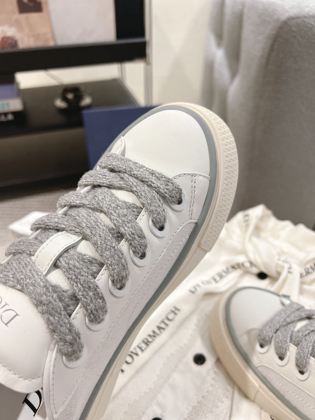 Low-top Dior sneaker close-up, white leather with gray lace eyelets and sole