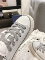 Low-top Dior sneaker close-up, white leather with gray lace eyelets and sole