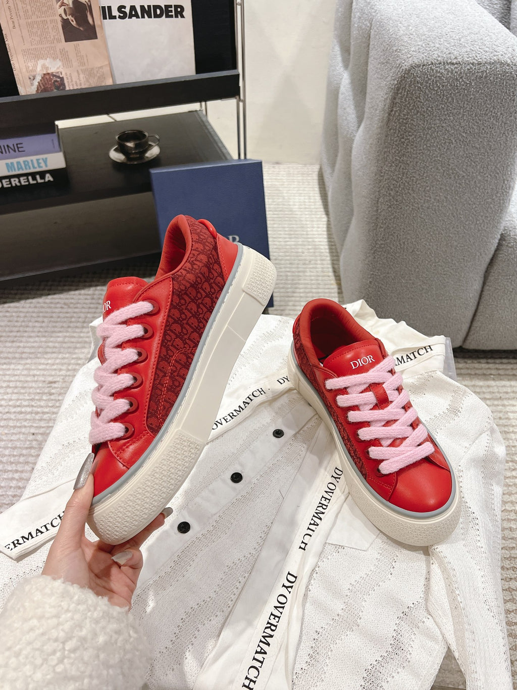 Red Dior low-top sneakers held in hand, pink laces and textured upper