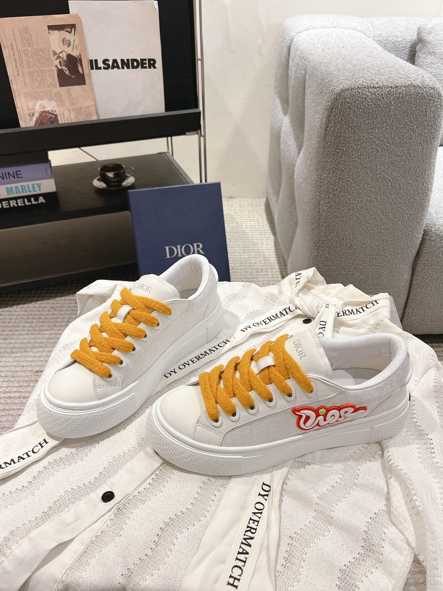 Pair of white Dior sneakers with mustard laces on a garment cover