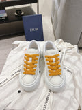 White Dior low-top sneakers with mustard lace-up front and logo on tongue
