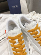 White Dior sneakers showing toe and lace eyelets with mustard laces