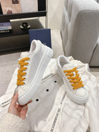 White Dior low-top sneakers with mustard laces and lace-up eyelets