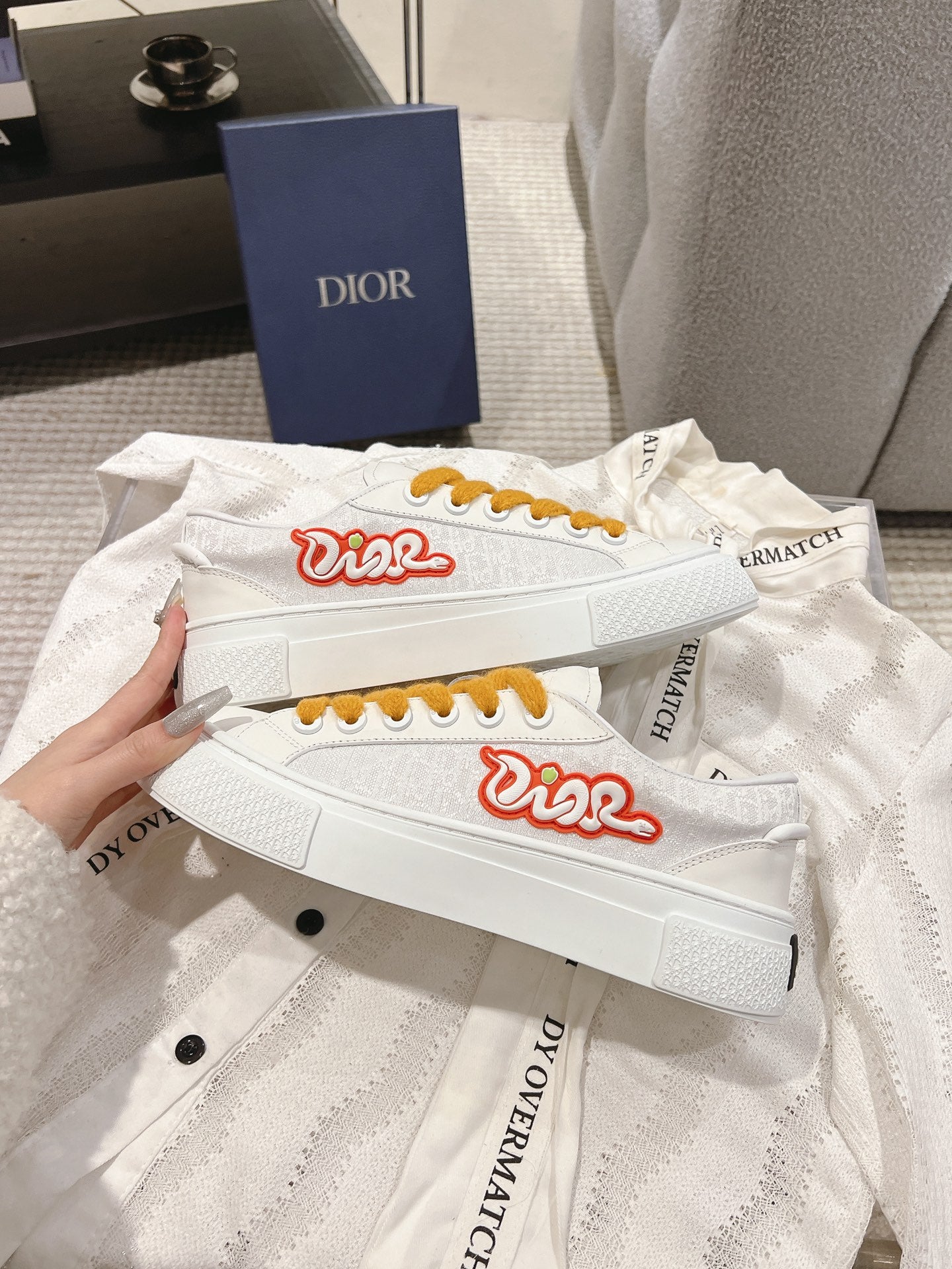 White Dior sneakers with red logo and mustard laces, side view