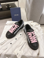 Black low-top sneakers with pink lace-up details on white dust bag
