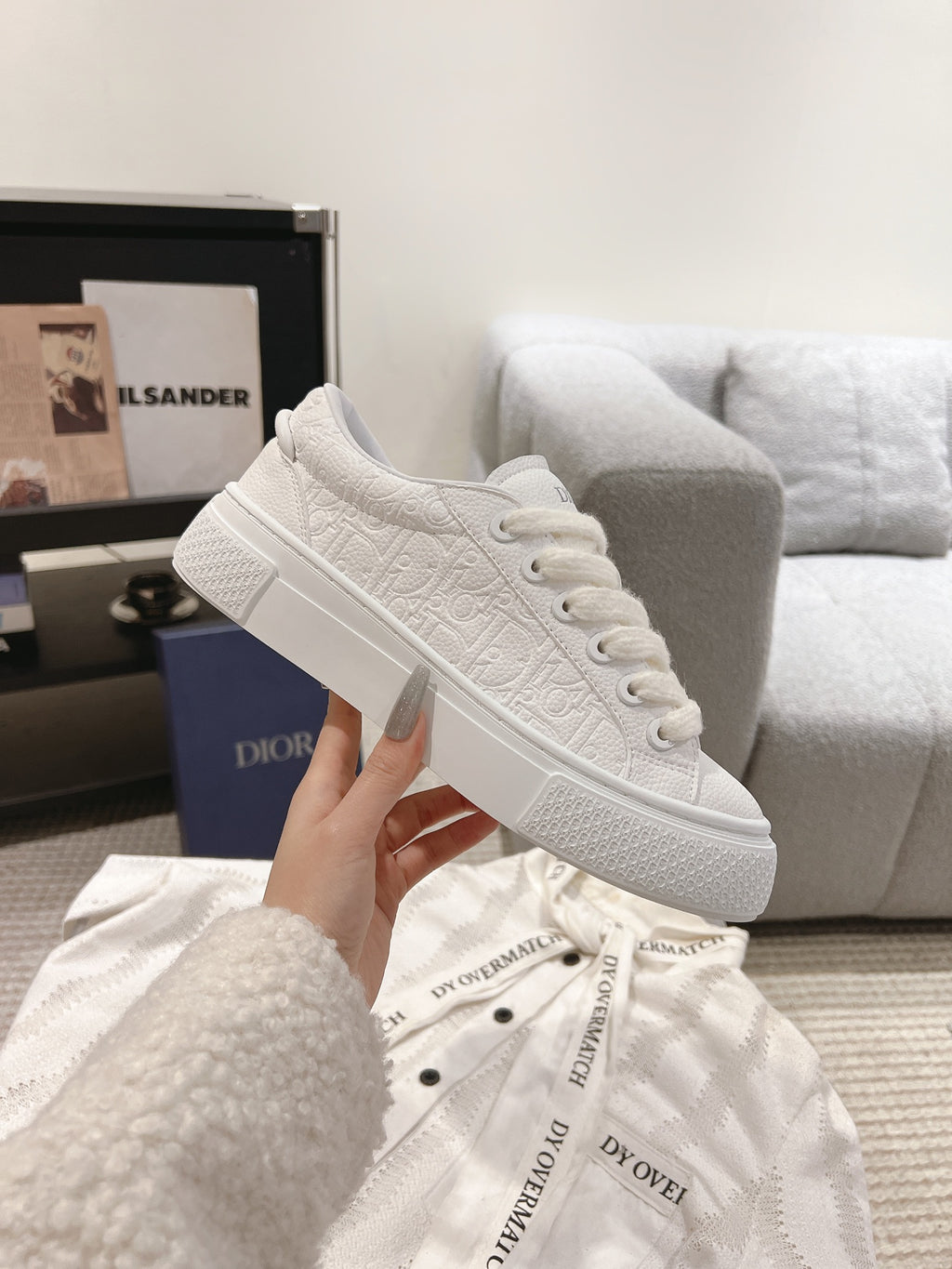 White low-top sneaker held up, showing lace-up front and textured upper