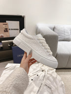 White low-top sneaker held up, showing lace-up front and textured upper