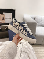 Navy and beige low-top sneakers with white laces and repeating logo print on sides