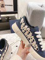 Navy low-top sneaker with white laces and beige logo embroidery on the side