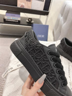 Black Dior low-top sneakers, angled side view with embossed logo pattern.