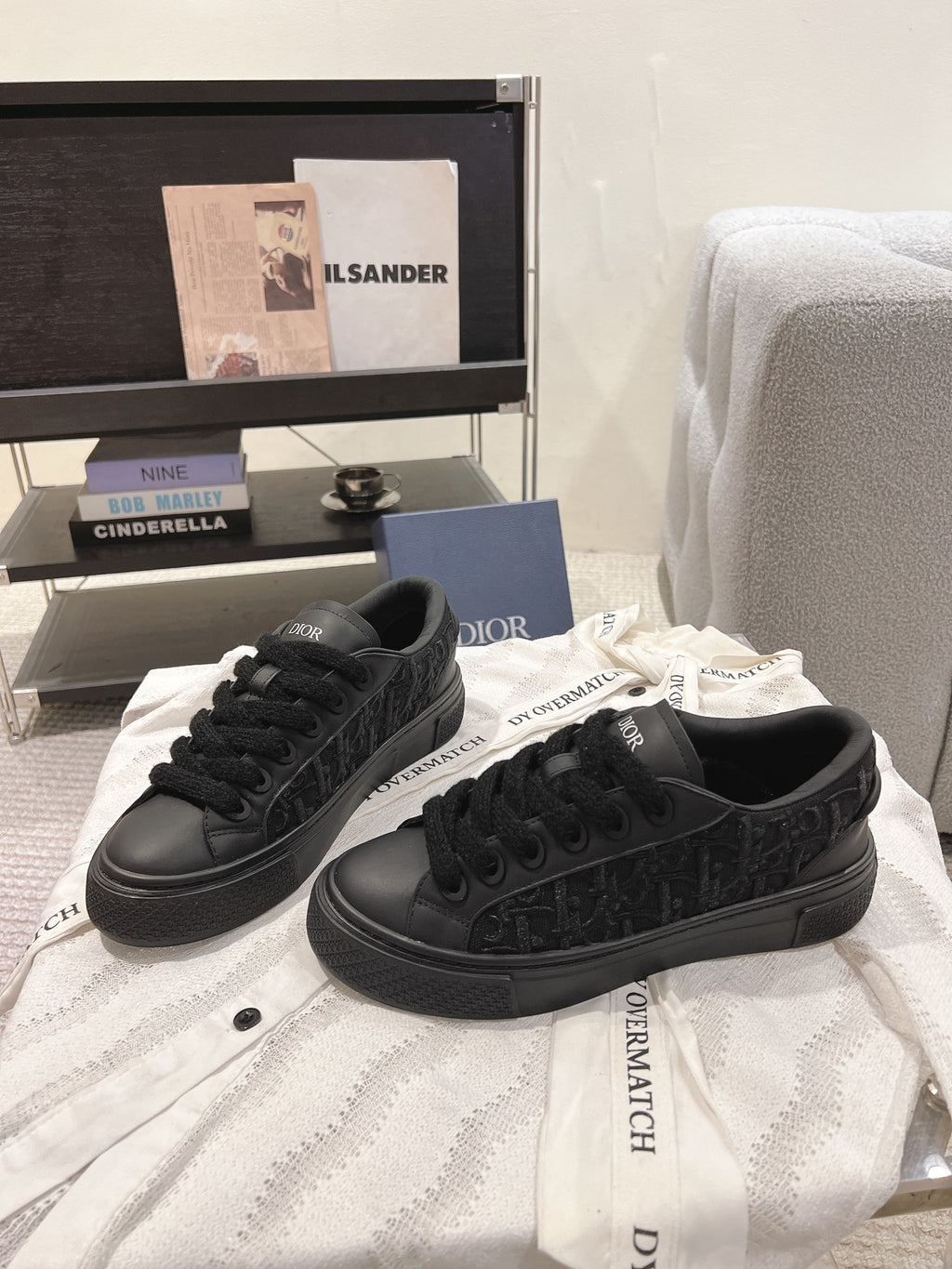 Black low-top Dior sneakers on white fabric with lace-up design.