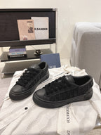 Black low-top Dior sneakers on white fabric with lace-up design.