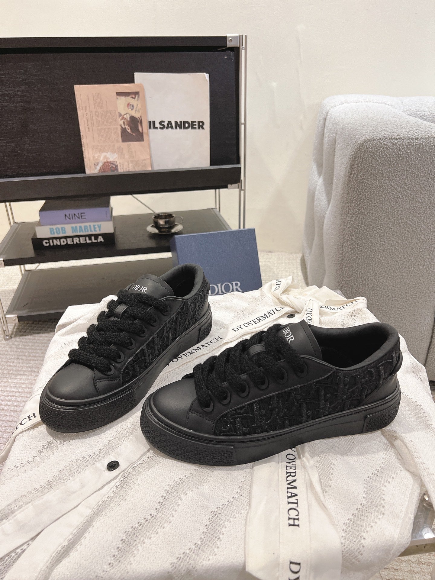 Black low-top Dior sneakers on white fabric with lace-up design.