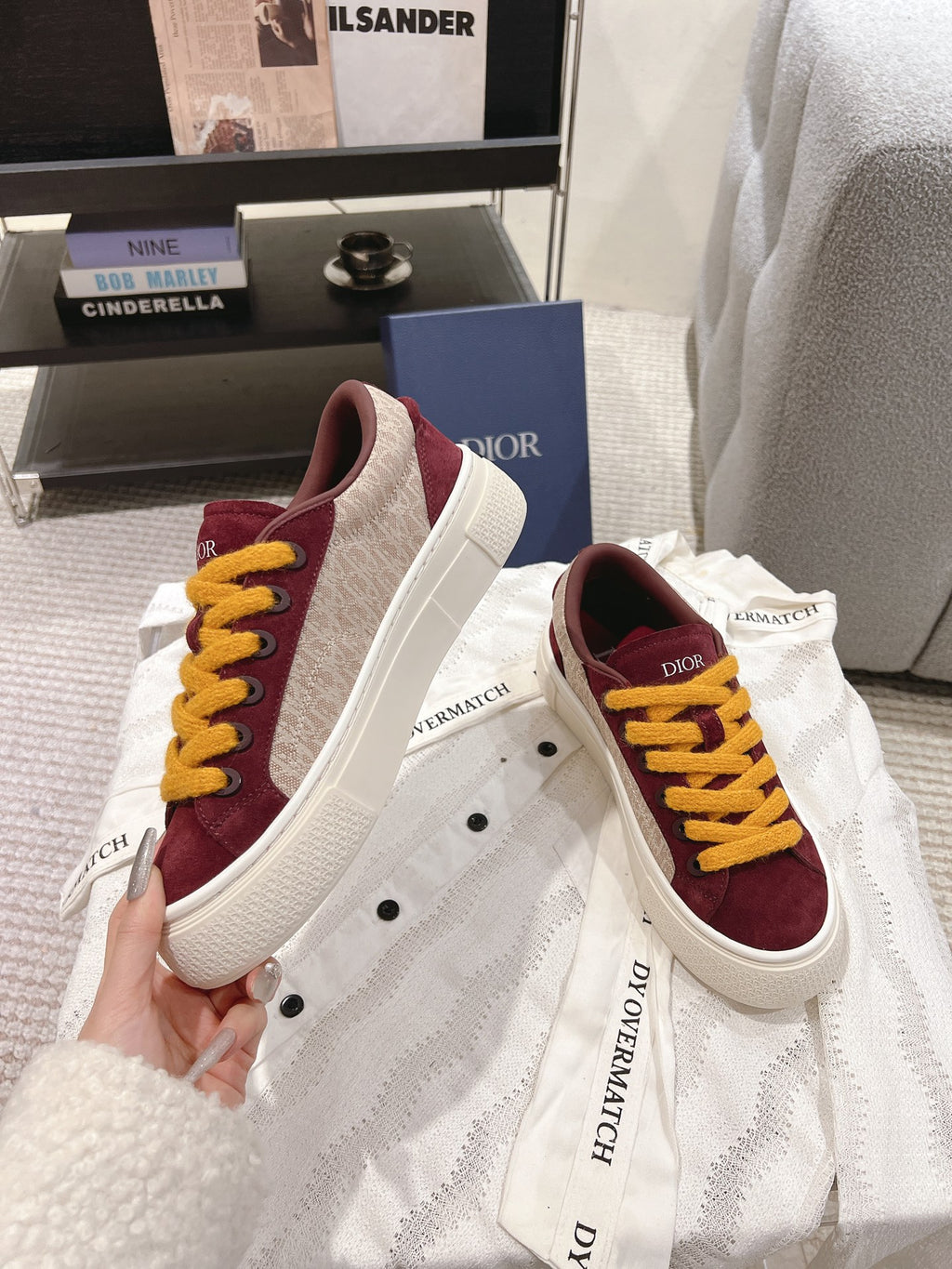Burgundy sneakers with yellow laces and white rubber sole, side view on garment cloth.