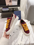 Burgundy sneakers with yellow laces and white rubber sole, side view on garment cloth.