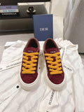 Burgundy low-top sneakers with yellow lace-up detail and white rubber sole, unisex.