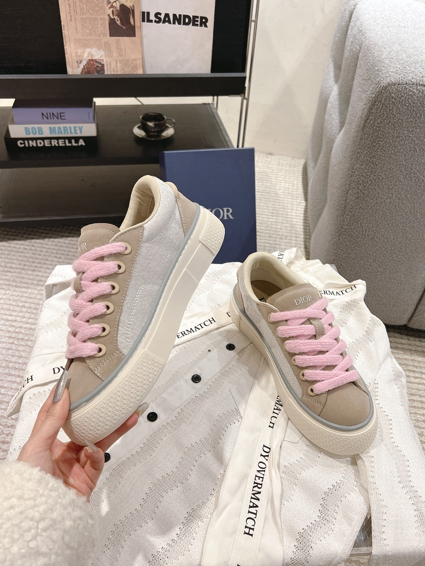 Hand-held pair of low-top sneakers in beige with pink laces and white sole, DIOR logo