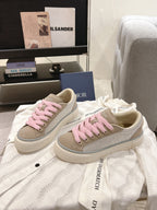 Pair of low-top sneakers in light beige with pink shoelaces and branded side trim
