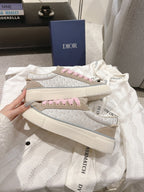 Two stacked low-top sneakers in light beige with pink laces and branded side stripe