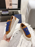 Tan low-top sneakers with blue laces and white soles, displayed on dust bag
