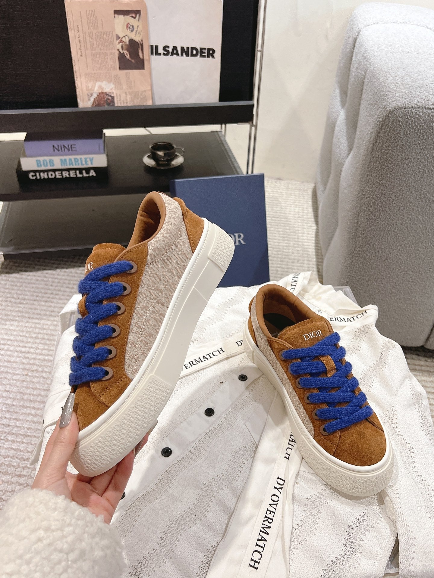 Tan low-top sneakers with blue laces and white soles, displayed on dust bag