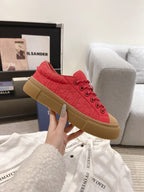 Red lace-up low-top sneaker held in hand, tan sole and toe detail visible